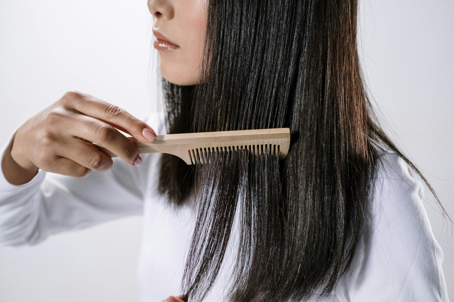 Woman gently combing long dark hair with a wooden comb to maintain scalp health and support results from a hair density serum.