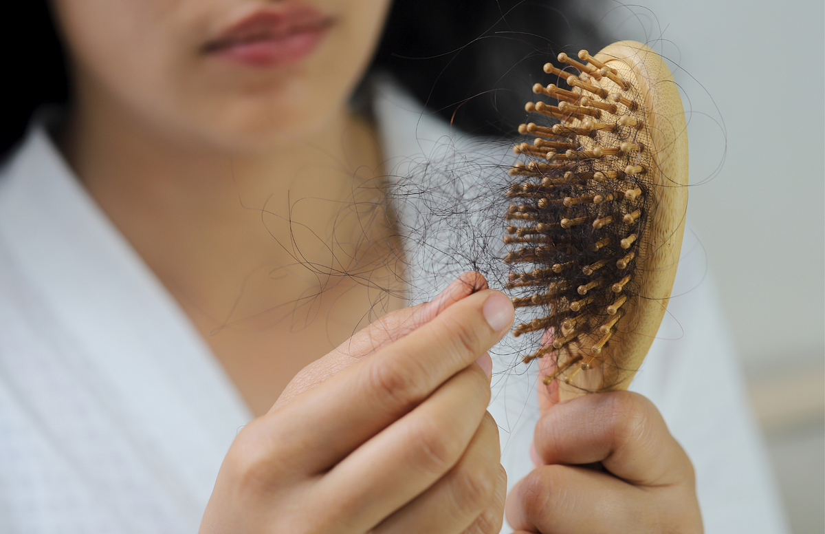 Woman examining thinning hair around her part during menopause, illustrating changes in hair density and the role of peptide and botanical scalp care.
