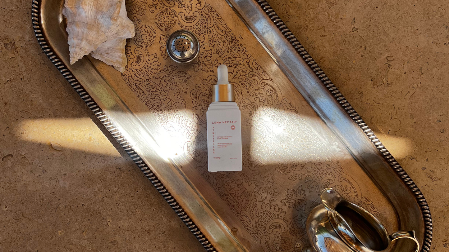 Luna Nectar Atmosphere Multi-Peptide Hair Density & Scalp Serum bottle on an antique silver tray, symbolizing luxury, clean chemistry, and investment in hair wellness.